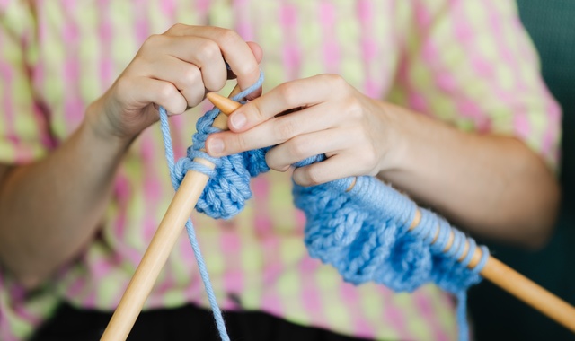 Close up of person knitting with blue wool and large needles