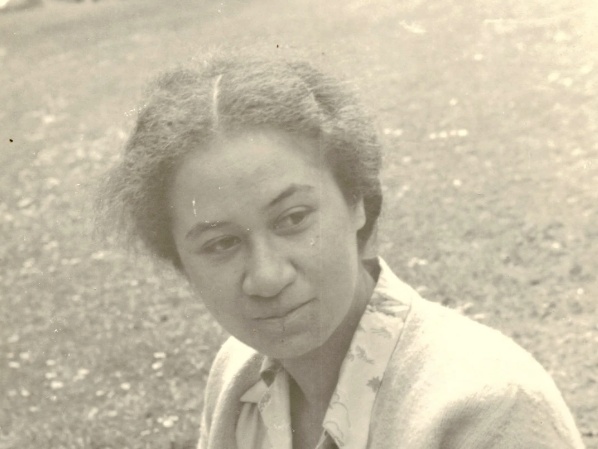 A vintage black‑and‑white photograph showing a person outdoors on grass, wearing a light‑colored collared shirt and jacket. The image has a soft, aged appearance with natural lighting and a shallow depth of field.